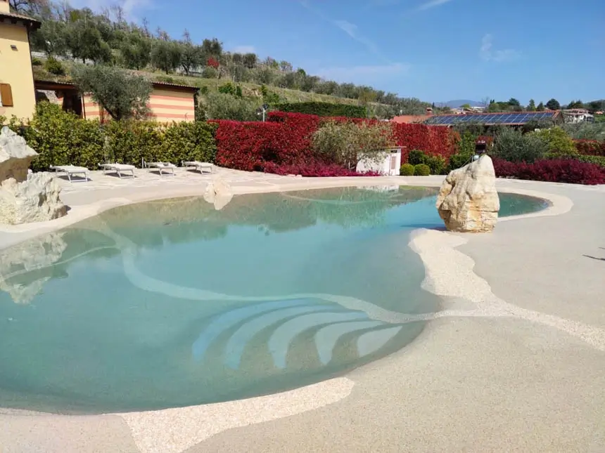 Sand pool with a sculptural boulder and red hedge