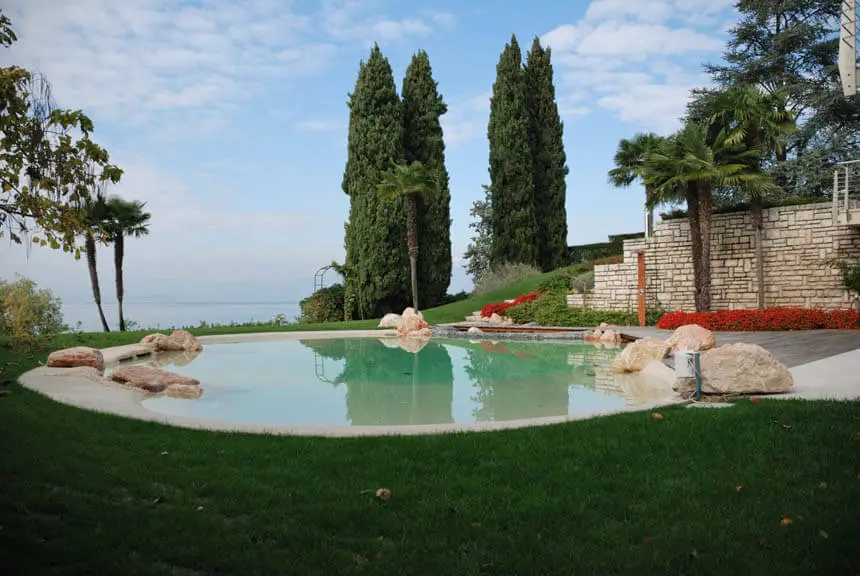 Sand pool on a lawn with tall cypress trees and a distant lake view