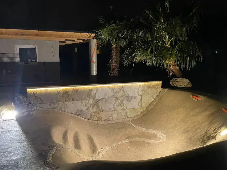 A hand-sculpted sand pool surface lit at night during construction